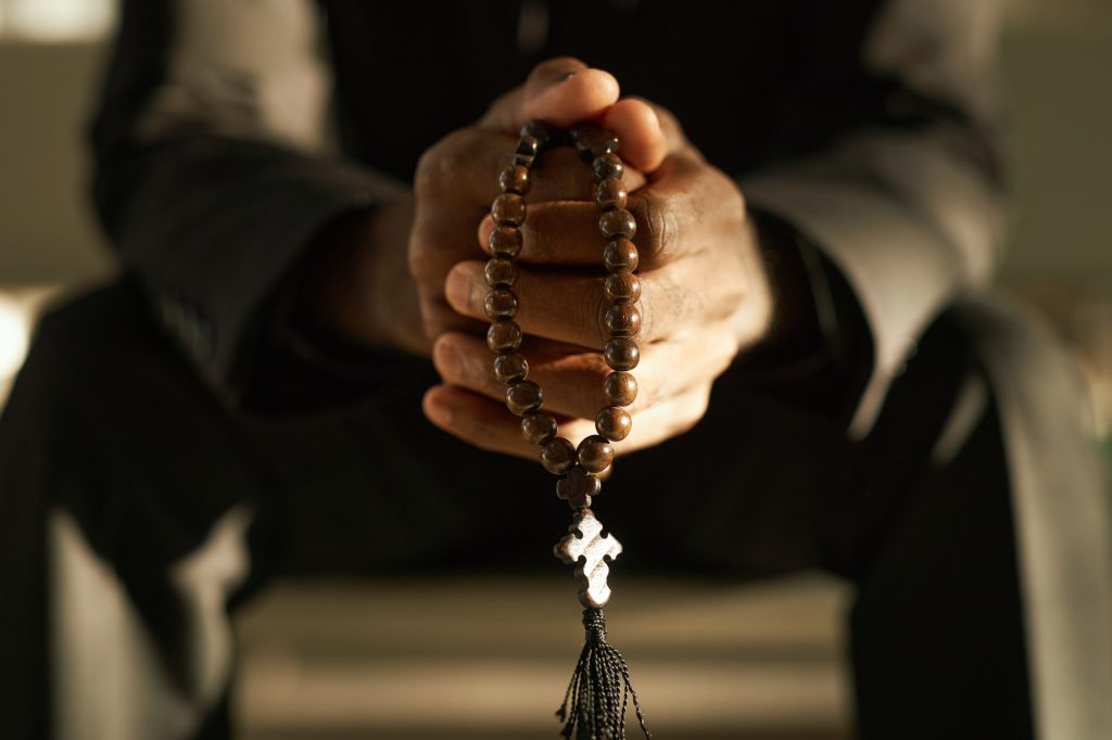 priest-holding-wooden-rosary-and-praying-in-sunlight.jpg